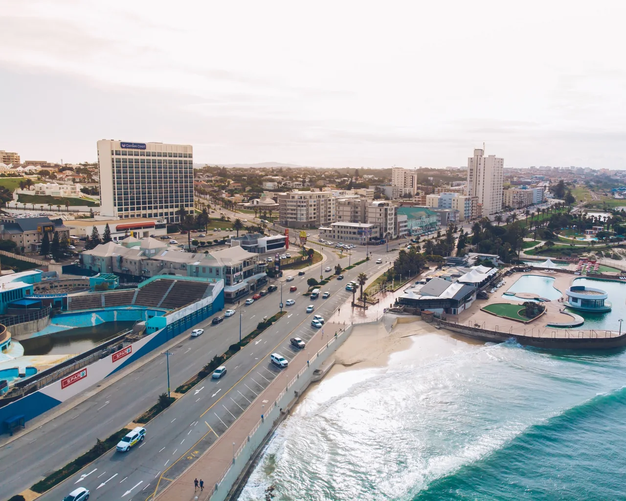 Aerial view of a coastal road, beachfront buildings and pools beside the ocean