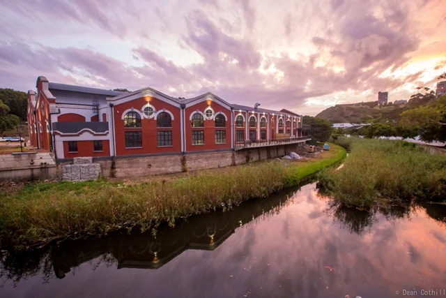 A red heritage building reflected in water in Gqeberha